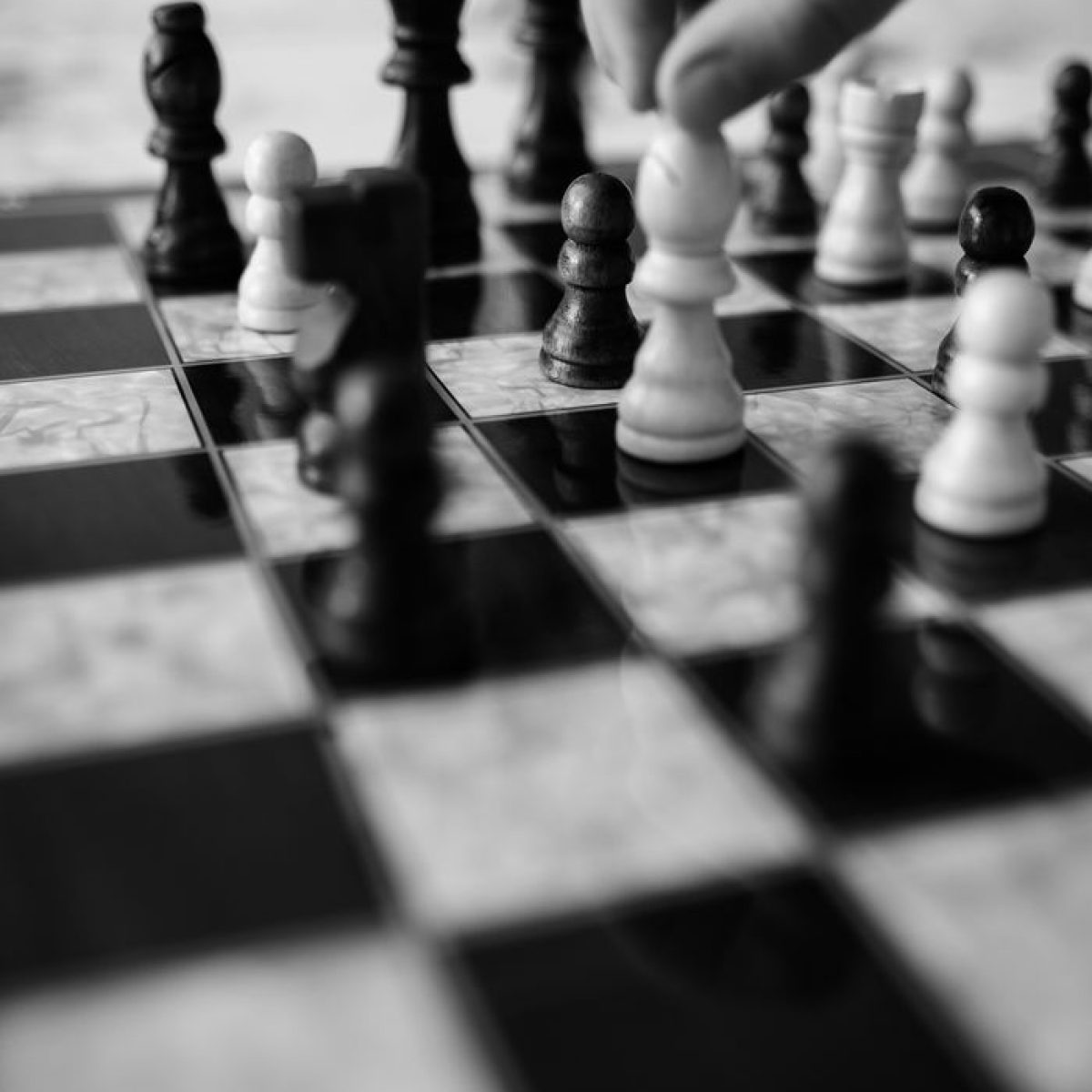 Black and white image of a hand moving chess pieces on a board, highlighting strategic play.