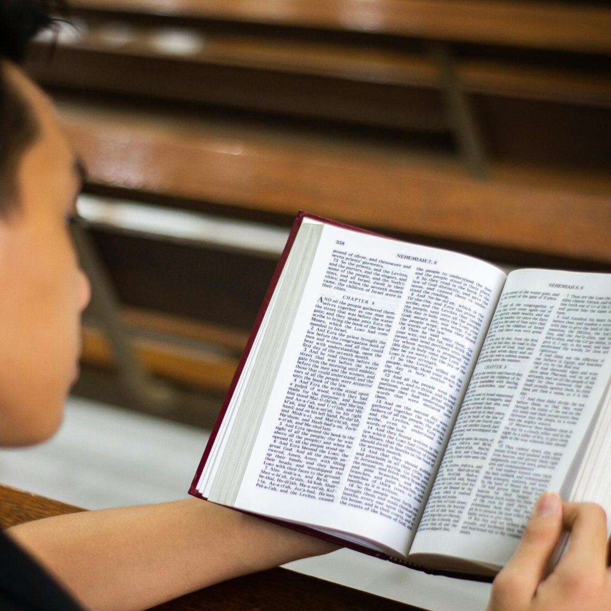 A man reading a book while sitting in a church interior, focusing on the open pages.