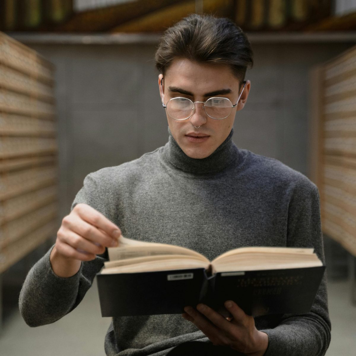 Young man in glasses reading a book in a library archive setting, focused on studying.